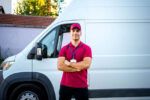 A fleet driver stands smiling in front of his company’s delivery van.