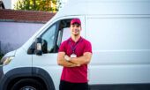 A fleet driver stands smiling in front of his company’s delivery van.