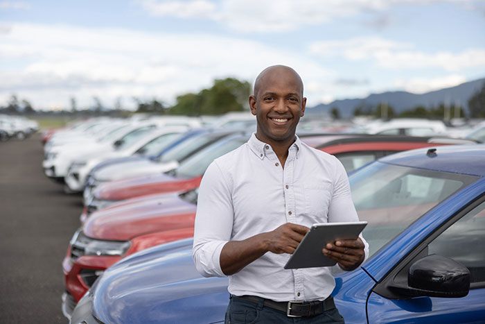 A business owner stands beside his fleet of vehicles reviewing the data collected on each individual vehicle from the fleet card app on his tablet.