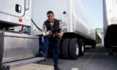 A business owner stands next to his fleet of semi trucks while holding his tablet.