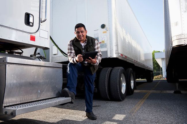 A business owner stands next to his fleet of semi trucks while holding his tablet.