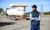 A happy truck driver stands outside his fleet vehicle while fueling at a gas station.
