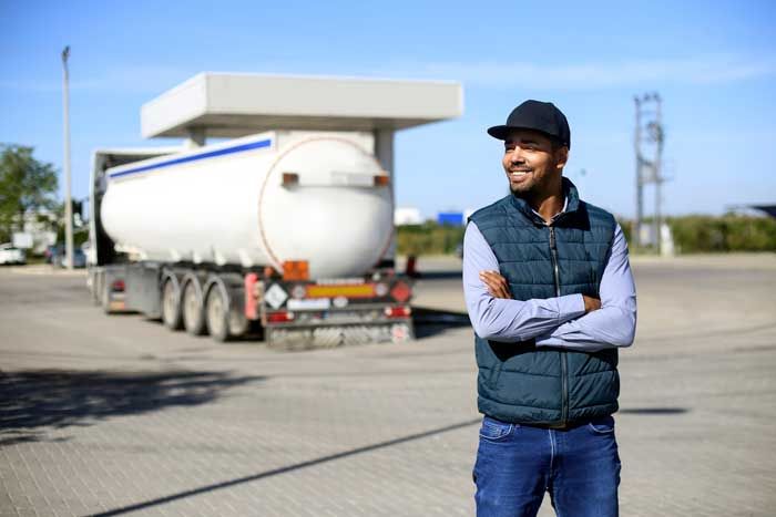 A happy truck driver stands outside his fleet vehicle while fueling at a gas station.