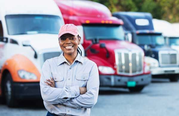 A small business owner stands smiling in front of her fleet of vehicles.