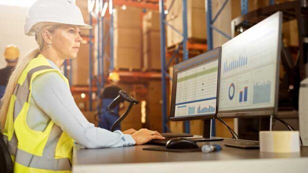 A fleet owner wears a hard hat while she checks and manages her fleet from her laptop on the worksite.