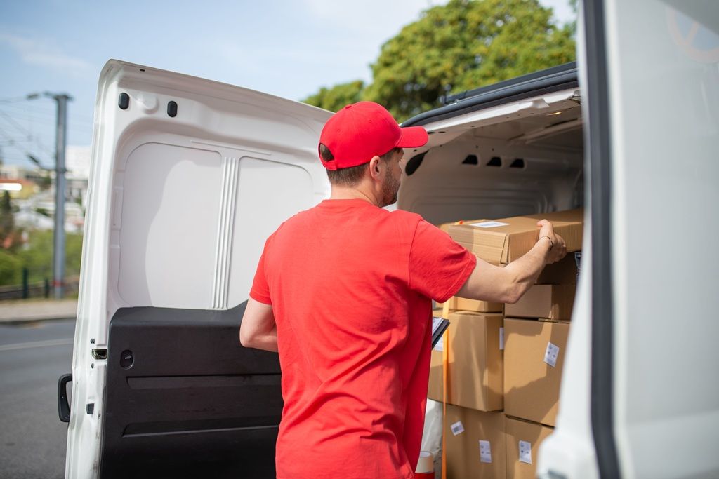 A fleet driver wearing a red shirt and red ball cap unloads boxes for delivery on his route.