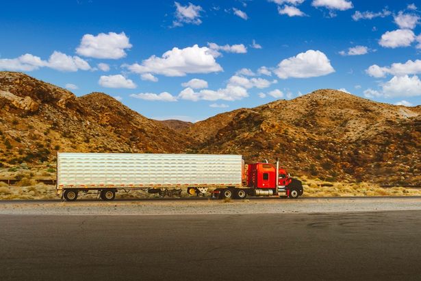 A semi-truck in full view with a rd cab parked outside a mountain range on its fleet route.